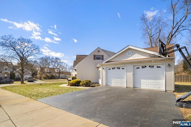 view of side of property featuring aphalt driveway, a yard, fence, and an attached garage