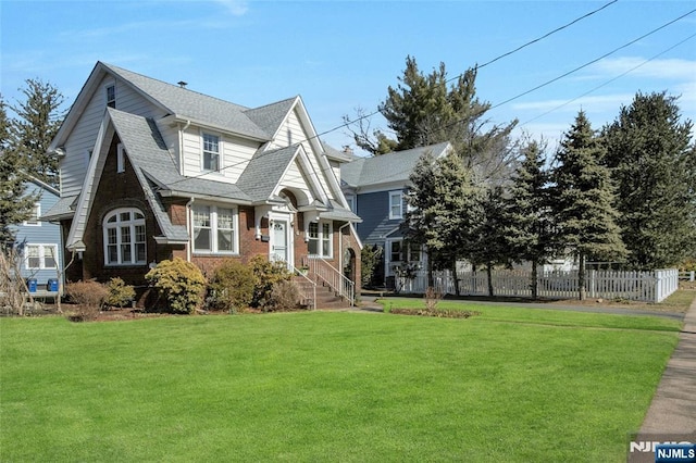 view of front facade featuring brick siding, roof with shingles, a front yard, and fence