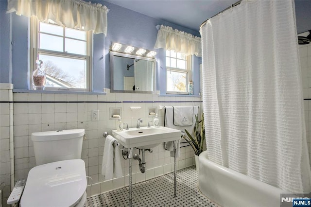 bathroom with tile patterned flooring, toilet, shower / bath combo with shower curtain, and tile walls