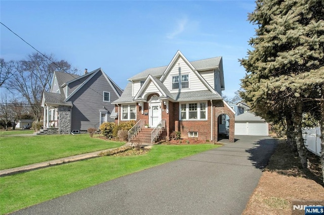 view of front of house with a front yard, a shingled roof, an outdoor structure, a garage, and brick siding