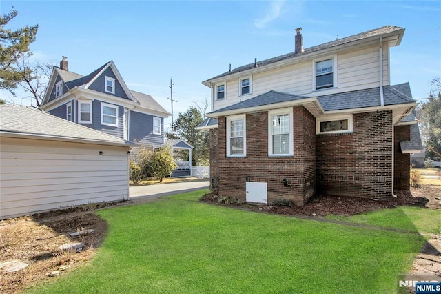 back of house featuring brick siding, a lawn, a chimney, and a shingled roof