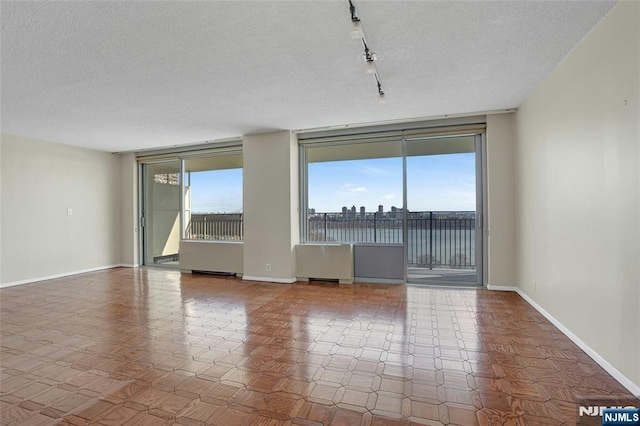 unfurnished room featuring track lighting, baseboards, and a textured ceiling