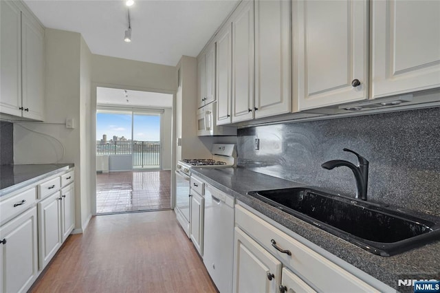 kitchen featuring white appliances, a sink, white cabinets, light wood-style floors, and tasteful backsplash