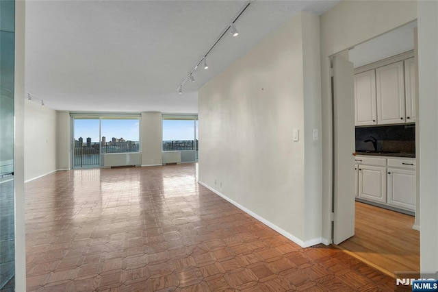 empty room featuring a city view, rail lighting, baseboards, and a sink