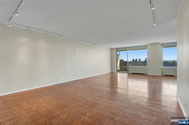 unfurnished room with track lighting, a view of city, and baseboards