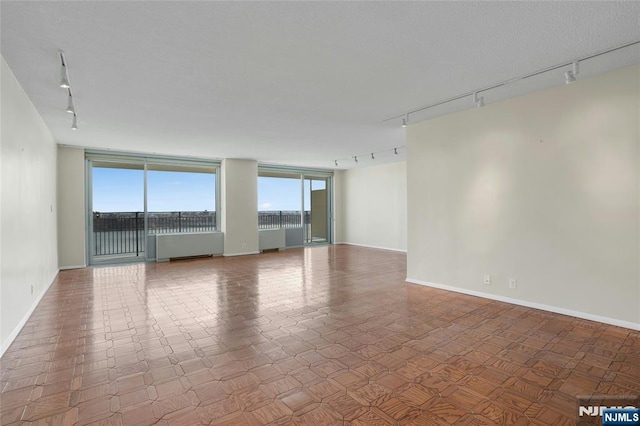 spare room featuring track lighting, radiator heating unit, and baseboards