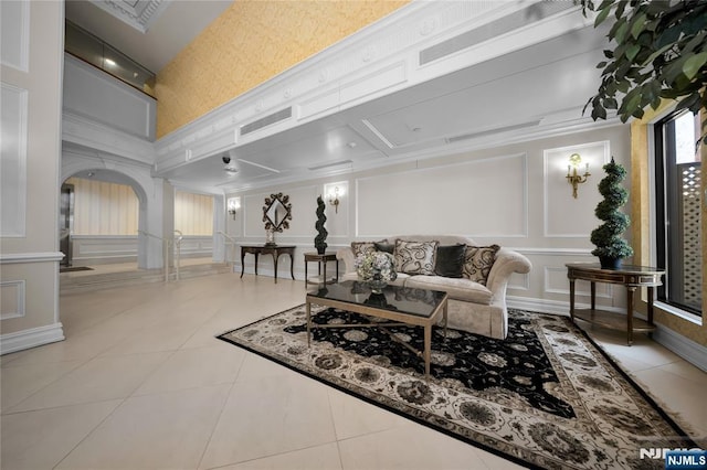 tiled living room with visible vents, crown molding, attic access, arched walkways, and a decorative wall