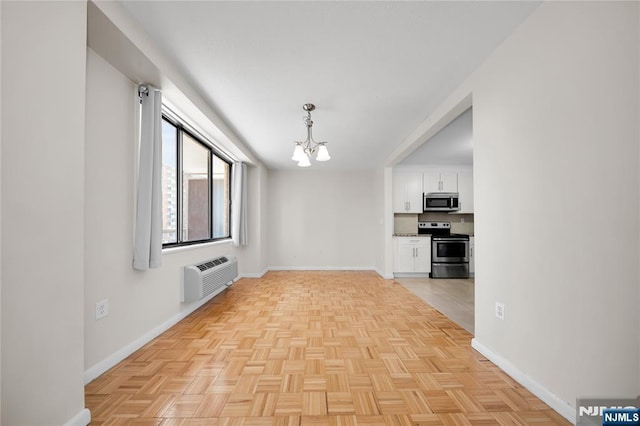 spare room featuring a notable chandelier, baseboards, and a wall mounted air conditioner