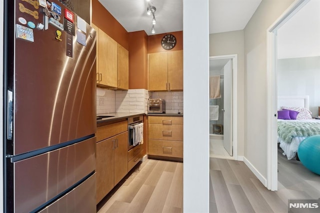 kitchen featuring dark countertops, backsplash, a toaster, appliances with stainless steel finishes, and light wood-style floors