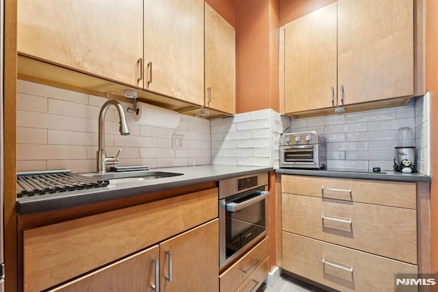 kitchen featuring light brown cabinetry, a sink, backsplash, a toaster, and stainless steel oven