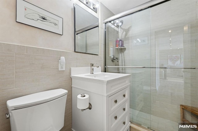 bathroom featuring toilet, tile walls, a stall shower, and vanity