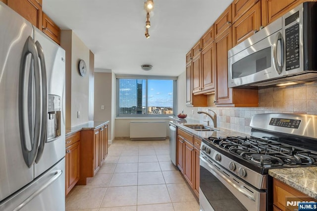 kitchen featuring light tile patterned floors, brown cabinetry, a sink, stainless steel appliances, and tasteful backsplash