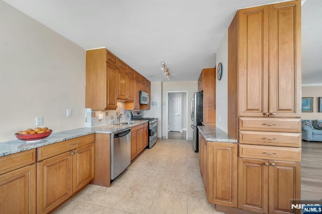 kitchen with brown cabinetry, stainless steel appliances, light stone countertops, and decorative backsplash