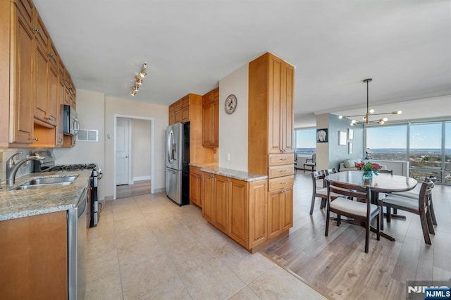 kitchen featuring pendant lighting, a sink, appliances with stainless steel finishes, brown cabinetry, and light stone countertops