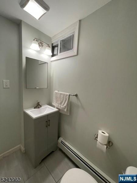 half bathroom with toilet, vanity, baseboards, baseboard heating, and tile patterned floors