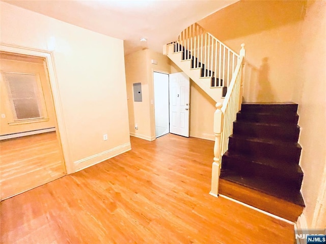 stairs featuring baseboard heating, wood finished floors, electric panel, and baseboards