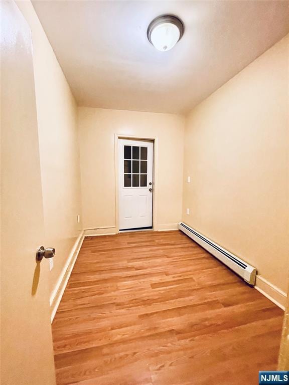 unfurnished room with a baseboard heating unit, light wood-type flooring, and baseboards