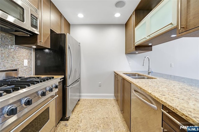 kitchen with stainless steel appliances, backsplash, a sink, light stone countertops, and baseboards