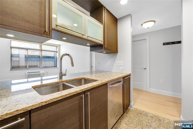 kitchen with a sink, baseboards, stainless steel dishwasher, light stone countertops, and glass insert cabinets