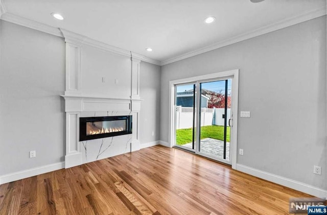 unfurnished living room with recessed lighting, a premium fireplace, wood finished floors, baseboards, and crown molding