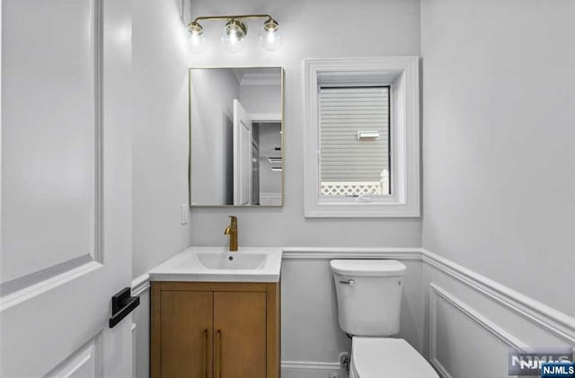 half bath featuring toilet, a wainscoted wall, a decorative wall, and vanity