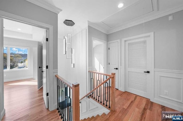 hallway with attic access, ornamental molding, wood finished floors, an upstairs landing, and a decorative wall