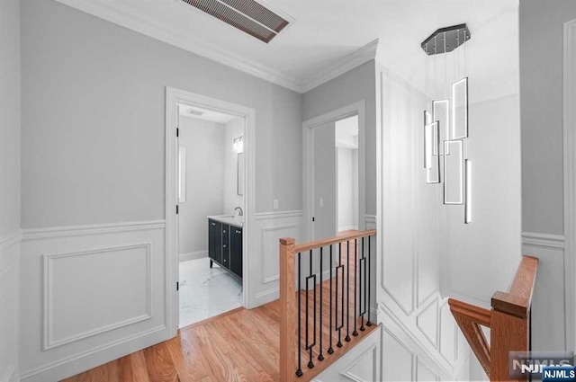 hall with light wood-style flooring, a decorative wall, an upstairs landing, visible vents, and crown molding