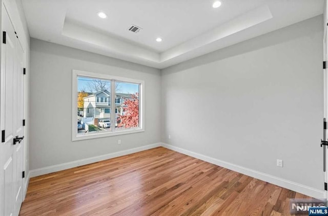 unfurnished bedroom featuring light wood-style floors, baseboards, a tray ceiling, and recessed lighting