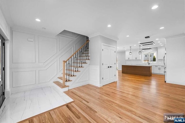 living area with stairs, crown molding, recessed lighting, and a decorative wall