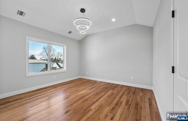 spare room with lofted ceiling, light wood finished floors, baseboards, and visible vents