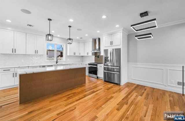 kitchen with light wood finished floors, wall chimney exhaust hood, appliances with stainless steel finishes, light countertops, and white cabinetry