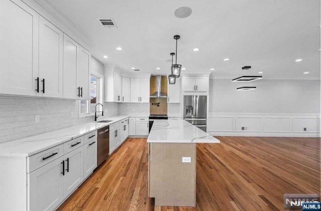 kitchen with stainless steel appliances, visible vents, a sink, a kitchen island, and wall chimney exhaust hood