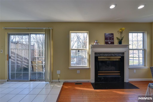 unfurnished living room featuring recessed lighting, a fireplace with flush hearth, plenty of natural light, and tile patterned flooring