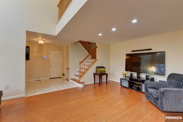 living room with stairway, wood finished floors, baseboards, recessed lighting, and a towering ceiling