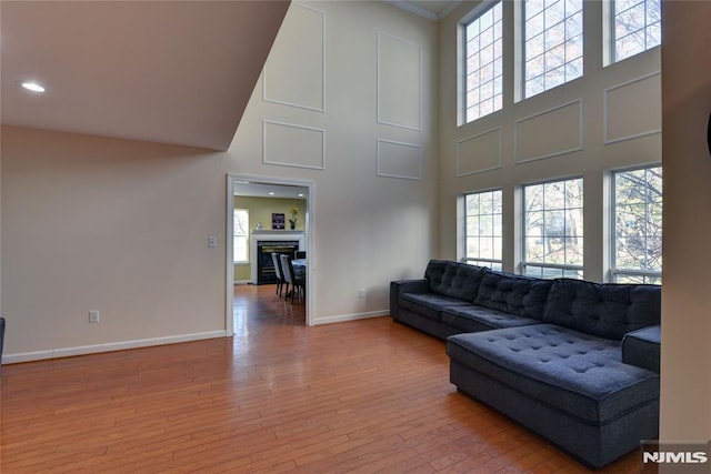 living area featuring a glass covered fireplace, a high ceiling, baseboards, and wood-type flooring