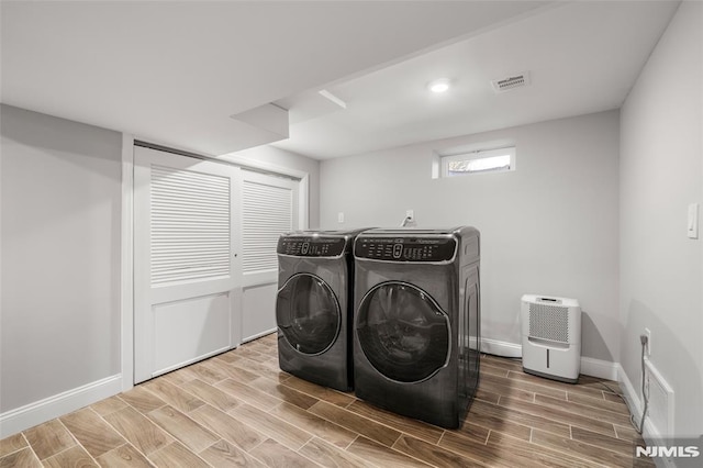 washroom featuring visible vents, baseboards, wood tiled floor, washer and clothes dryer, and laundry area