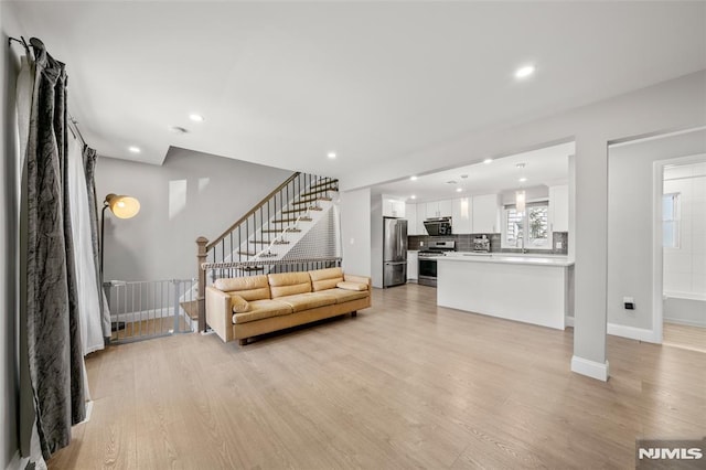 living area with recessed lighting, baseboards, light wood-style floors, and stairs