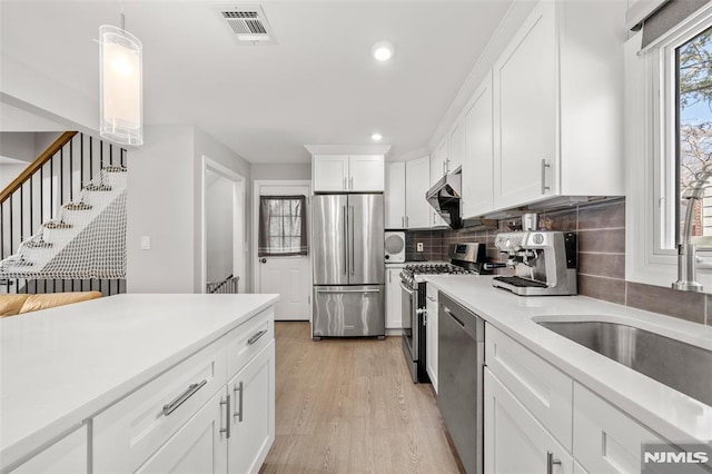 kitchen featuring light wood finished floors, visible vents, under cabinet range hood, light countertops, and stainless steel appliances