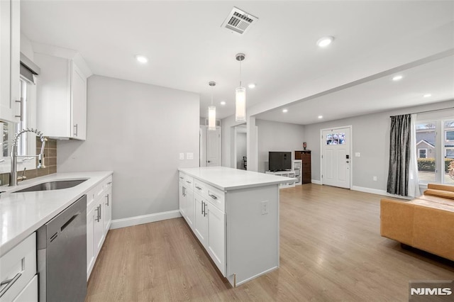 kitchen featuring visible vents, a sink, stainless steel dishwasher, open floor plan, and a peninsula