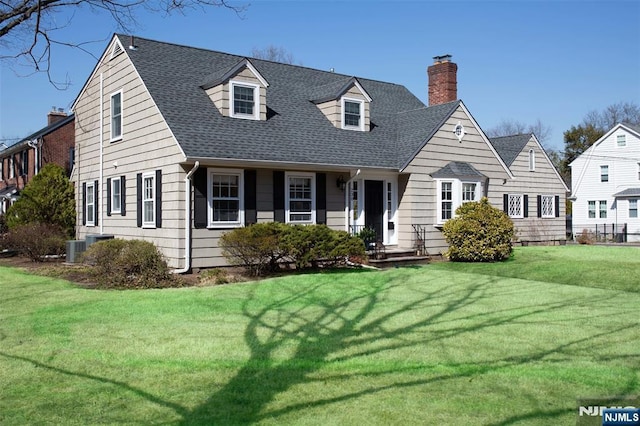 new england style home featuring a chimney, a shingled roof, and a front yard