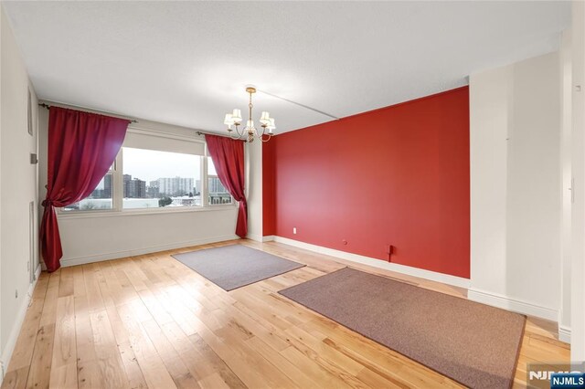 unfurnished room with a chandelier, wood-type flooring, a city view, and baseboards