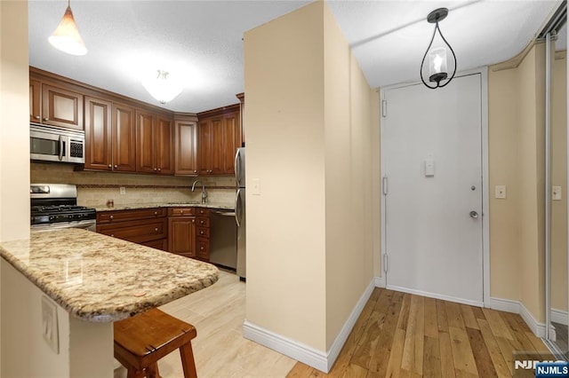 kitchen featuring stainless steel appliances, light wood finished floors, a peninsula, and backsplash