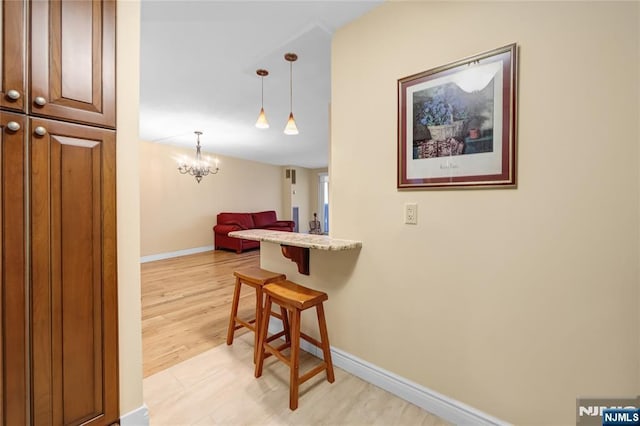 hall featuring a chandelier, light wood-type flooring, and baseboards