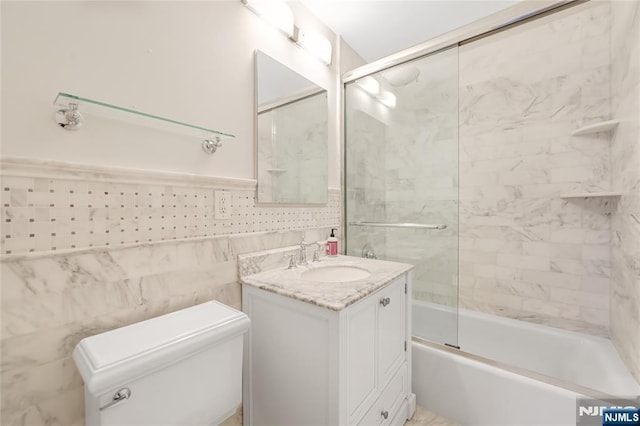 full bathroom with a wainscoted wall, tile walls, toilet, combined bath / shower with glass door, and vanity