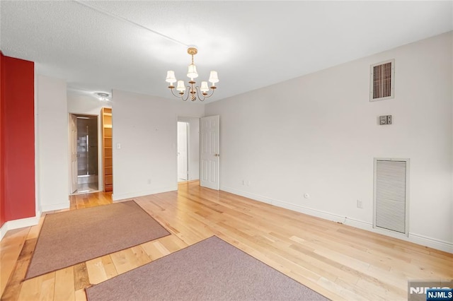 interior space with a chandelier, light wood-style flooring, visible vents, and baseboards