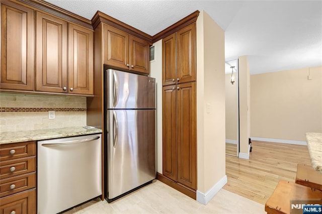 kitchen with tasteful backsplash, brown cabinetry, light wood-style flooring, light stone counters, and stainless steel appliances