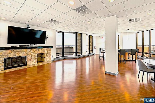 unfurnished living room with expansive windows, a stone fireplace, wood finished floors, and visible vents