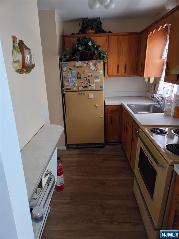 kitchen with white range with electric stovetop, light countertops, dark wood-type flooring, freestanding refrigerator, and a sink