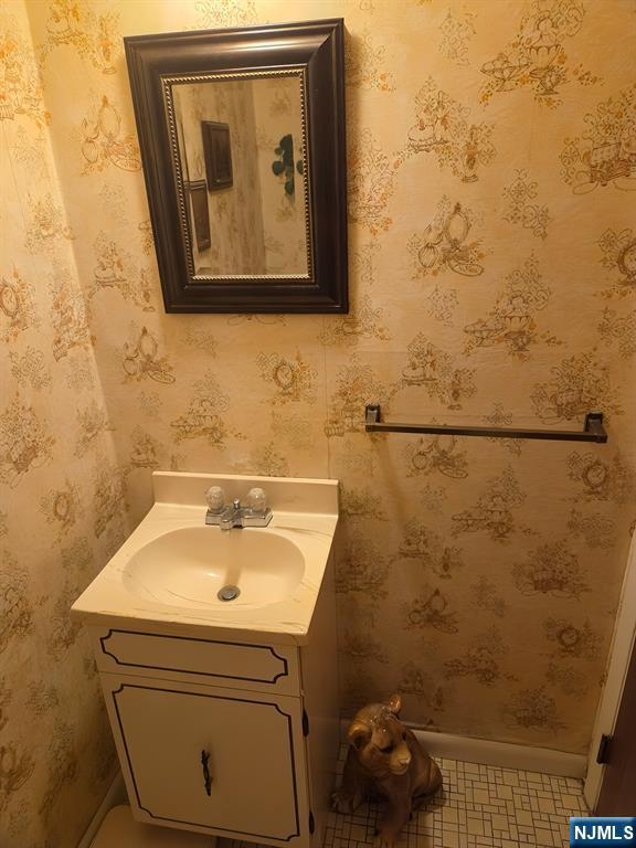 bathroom with baseboards, vanity, and wallpapered walls