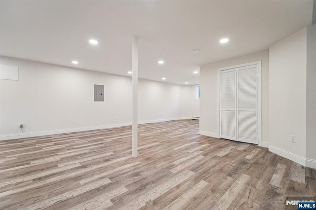 finished basement with light wood finished floors, baseboards, electric panel, baseboard heating, and recessed lighting